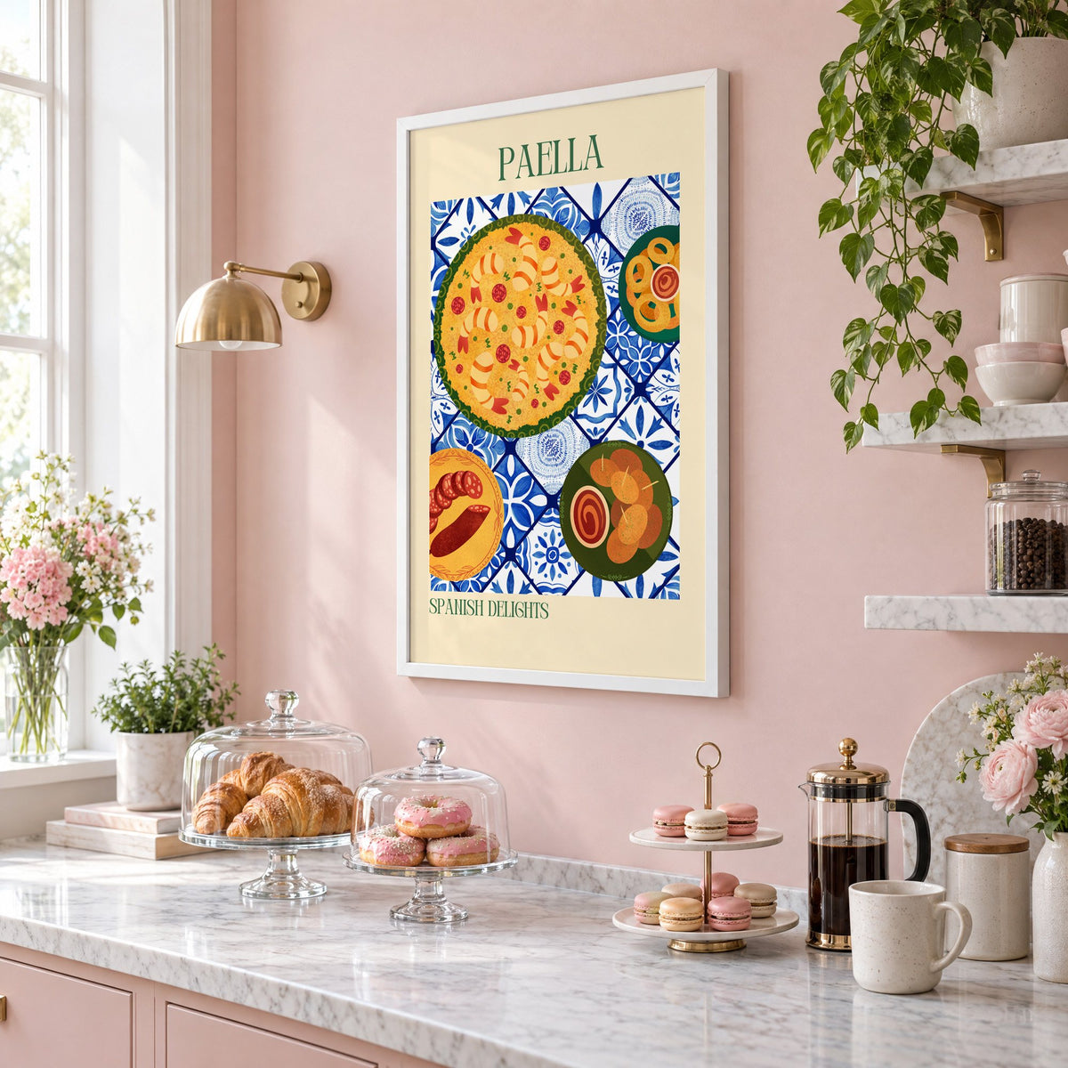 PAELLA Spanish Delights tapas tile table print in a white frame on a blush pink wall above a patisserie counter with croissants and macarons, seen at an angle