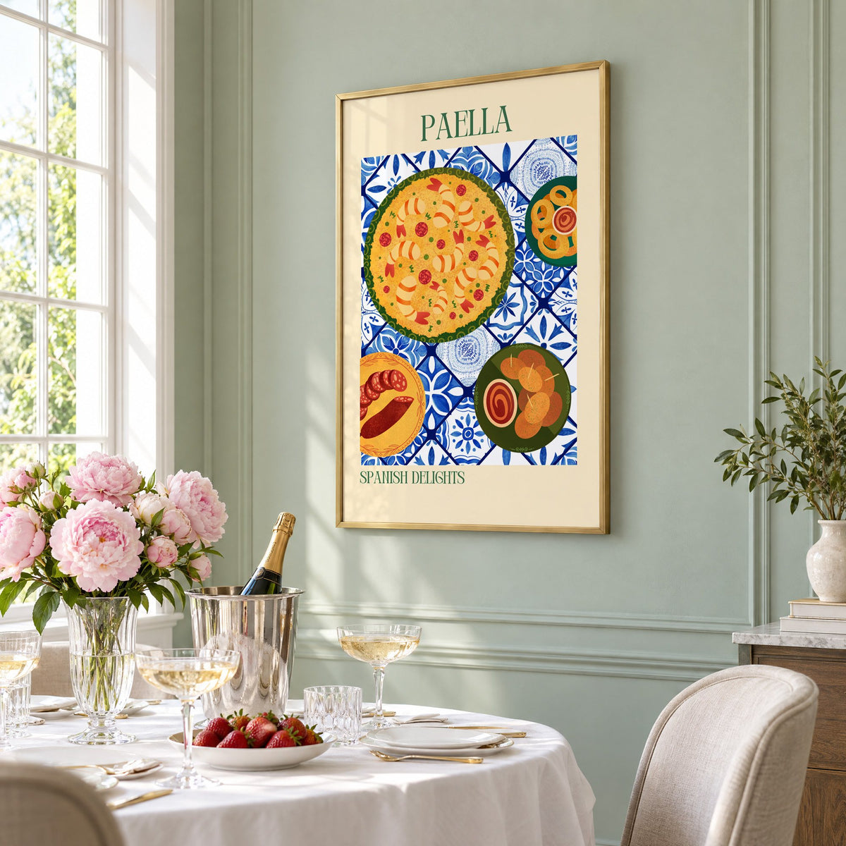 PAELLA Spanish Delights tapas tile table print in a brass frame on a sage wall above a brunch table with champagne and peonies, seen at an angle