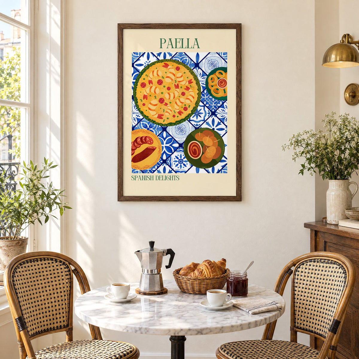 PAELLA Spanish Delights tapas tile table print in a walnut frame above a marble bistro table with croissants and rattan chairs