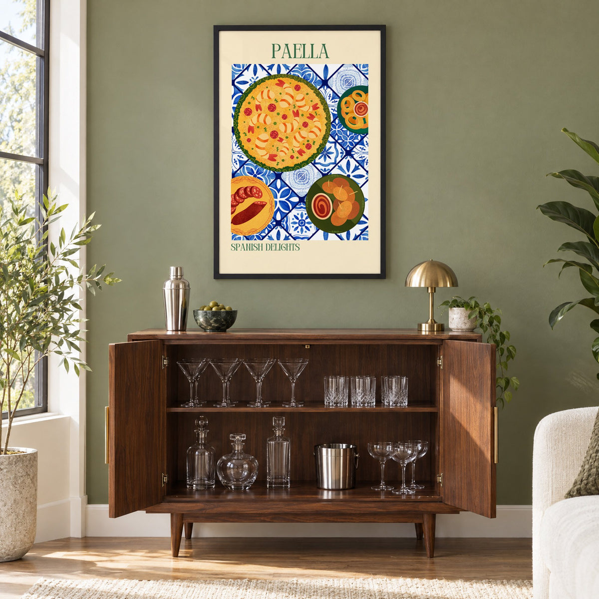 PAELLA Spanish Delights tapas tile table print in a black frame on an olive green wall above a walnut bar cabinet with glassware