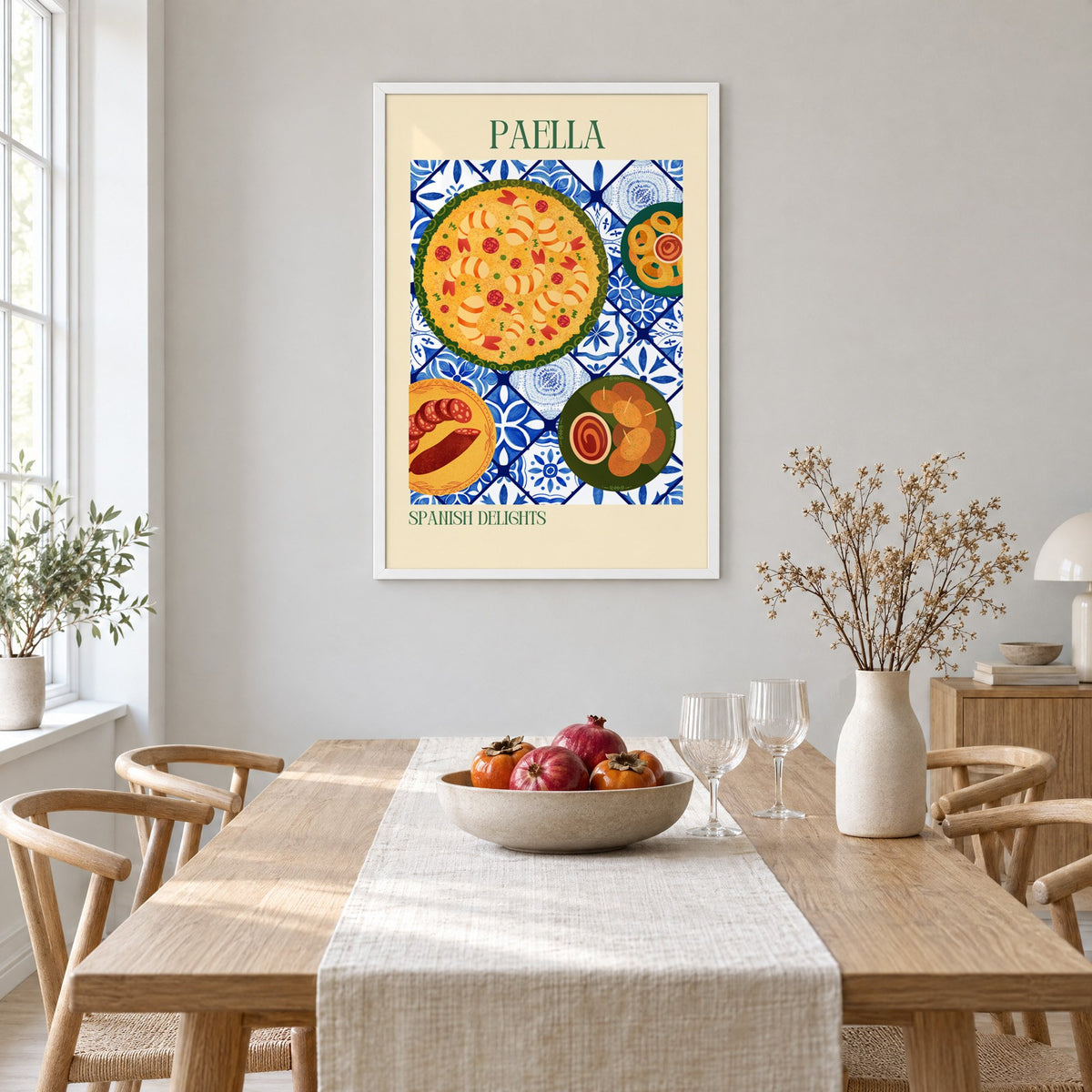 PAELLA Spanish Delights tapas tile table print in a white frame above a light oak dining table with a linen runner and fruit bowl