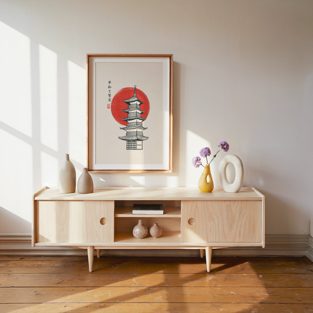 pagoda line art with red sun print shown in a wood frame with a white mat above a pale wood media console