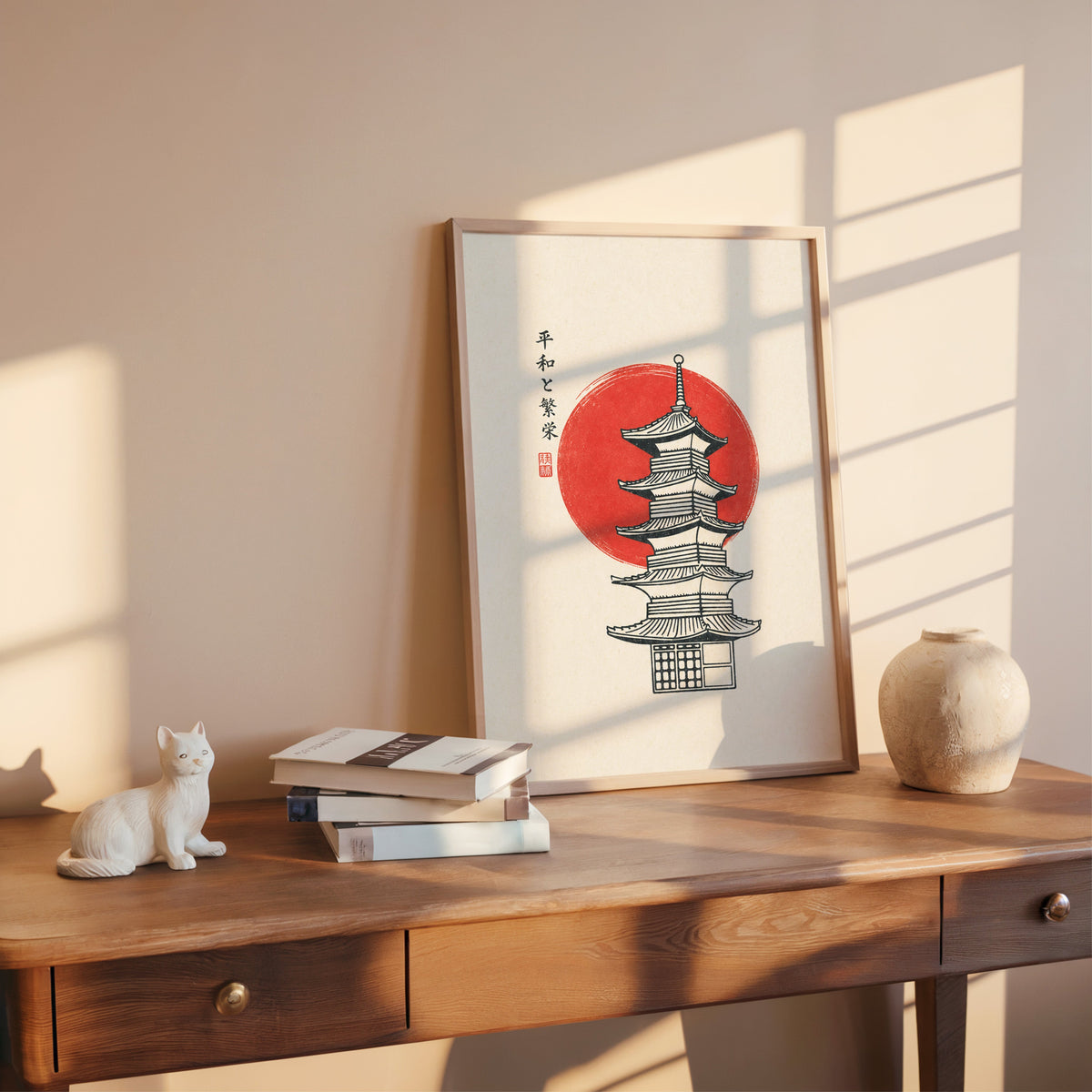 pagoda line art with red sun print shown in a rose gold frame leaning on a wooden writing desk with books
