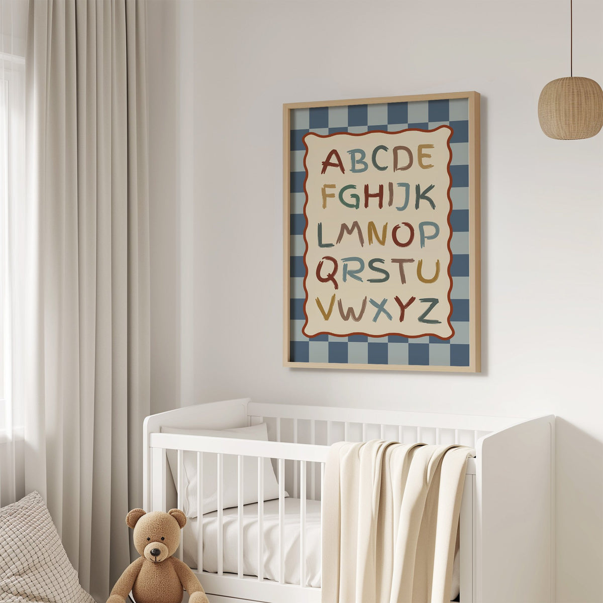 Painted alphabet wavy frame nursery print in an oak frame above a white crib with a teddy bear