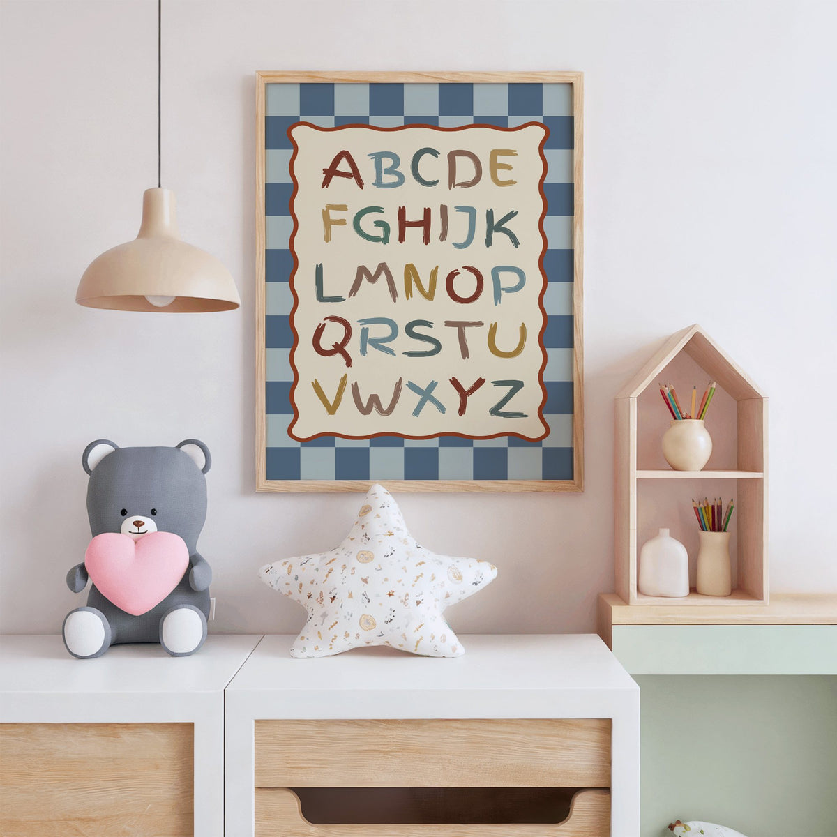 Painted alphabet wavy frame nursery print in an oak frame above a white dresser with a star pillow and house shelf