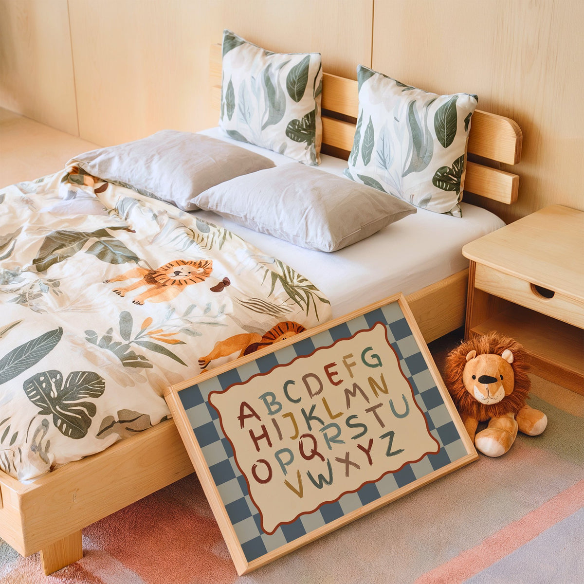Landscape painted alphabet wavy frame nursery print in an oak frame leaning on a kids bed by a lion plush