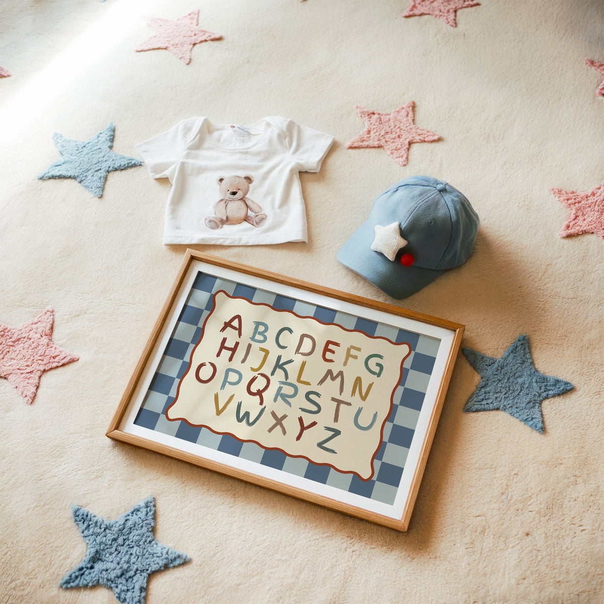 Landscape painted alphabet wavy frame nursery print in a matted oak frame on a star rug with a baby tee