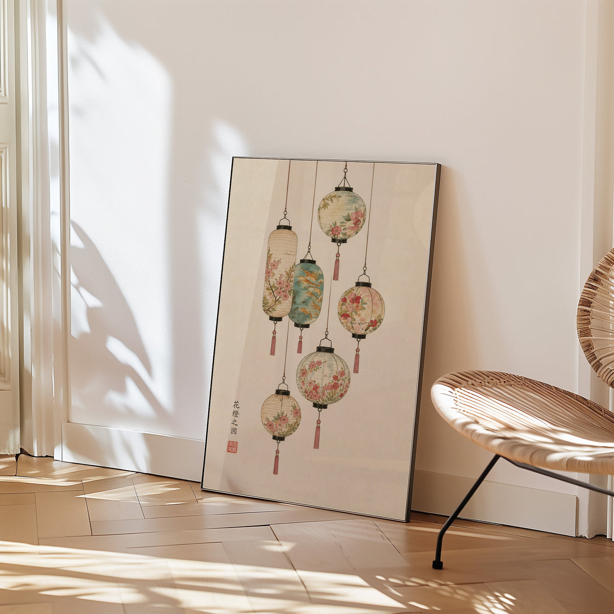 painted paper lanterns with flowers print in a black frame leaning on a herringbone floor beside a woven rattan chair