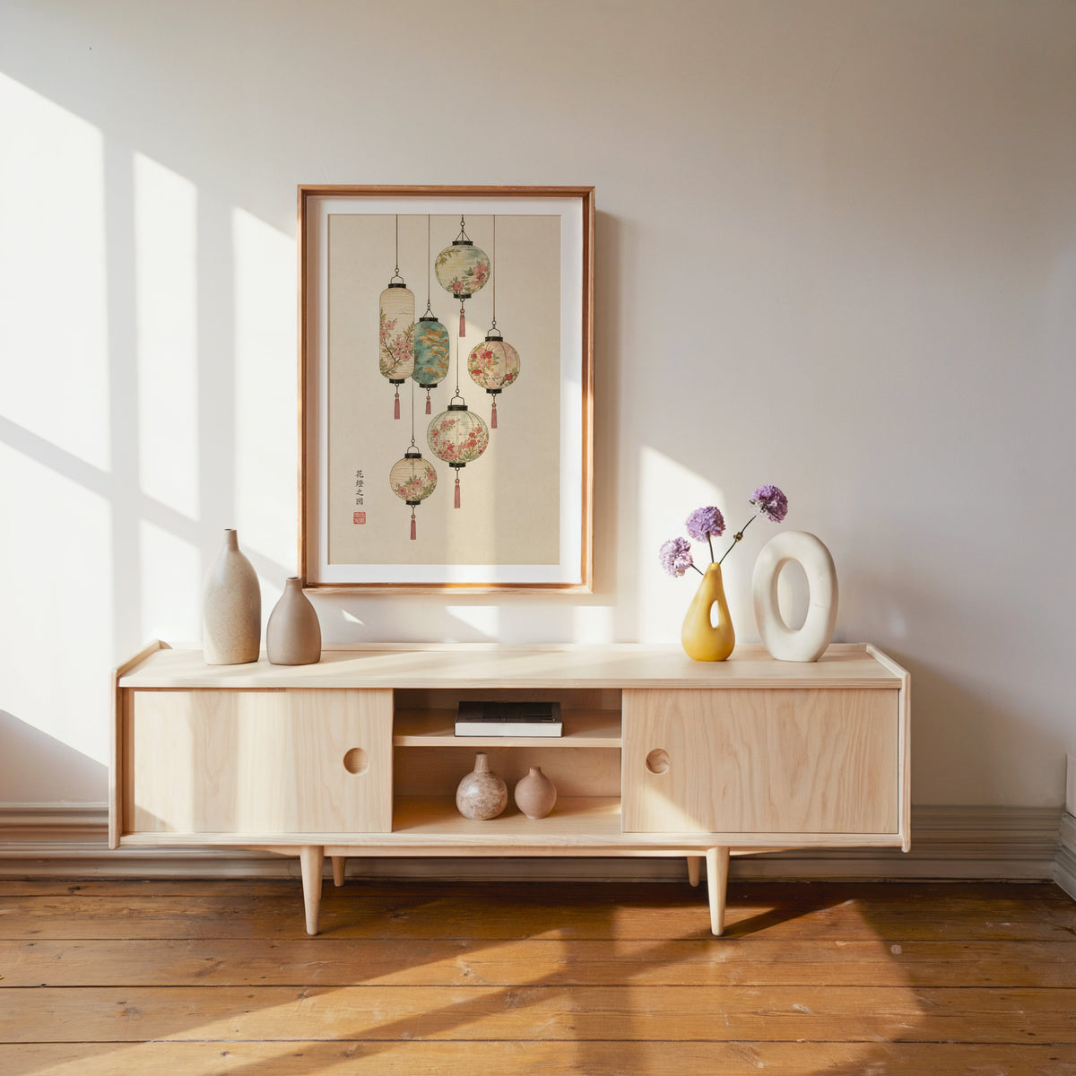 painted paper lanterns with flowers print shown in a wood frame with a white mat above a pale wood media console