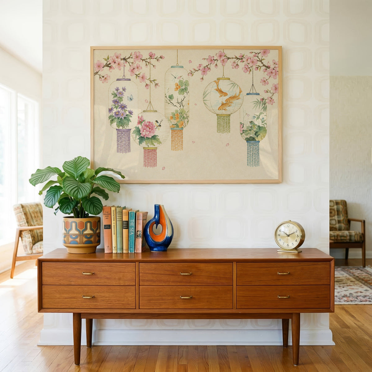 Five painted lanterns under cherry blossom print in a light oak frame above a teak credenza with books and a brass clock