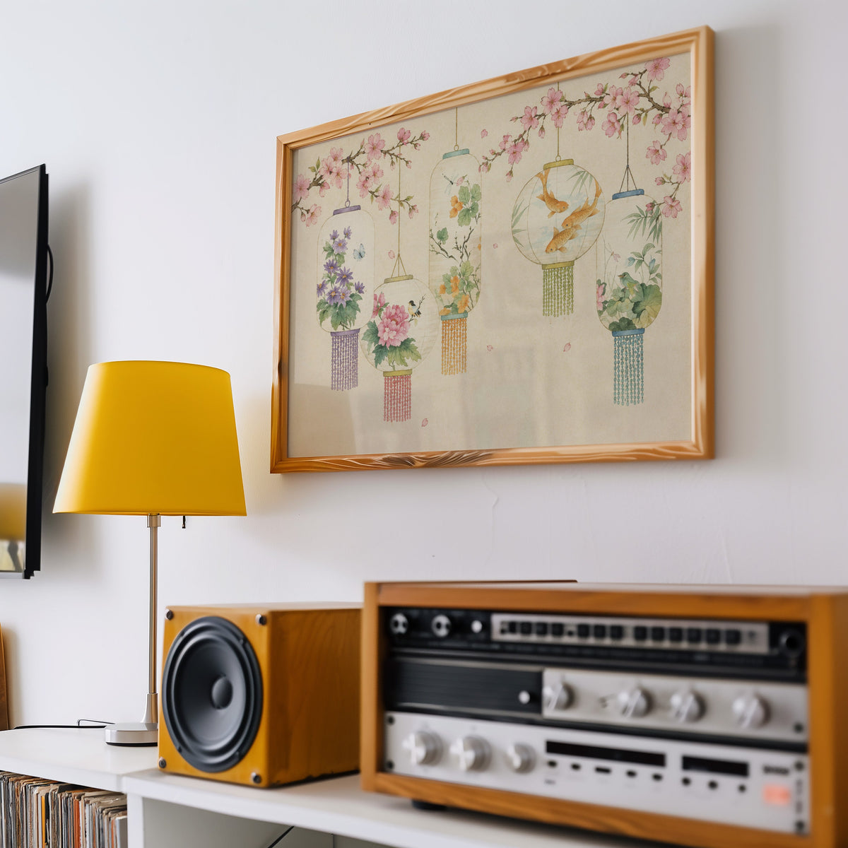 Five painted lanterns under cherry blossom print in a pine frame above a vintage stereo and a yellow table lamp