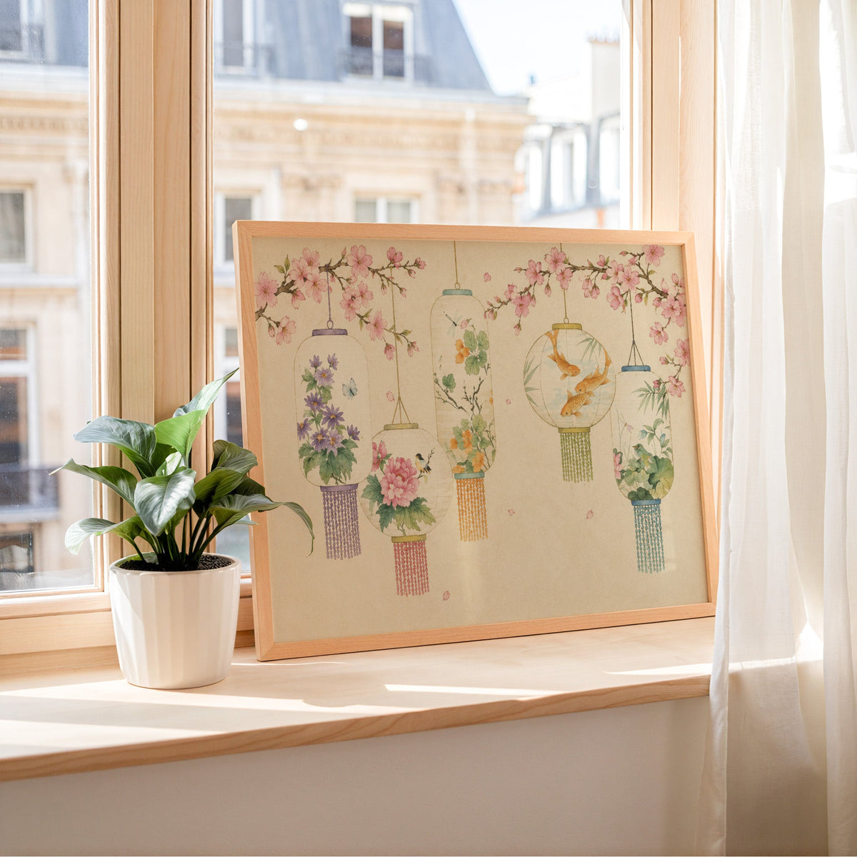 Five painted lanterns under cherry blossom print in a light wood frame leaning on a sunny windowsill by sheer curtains