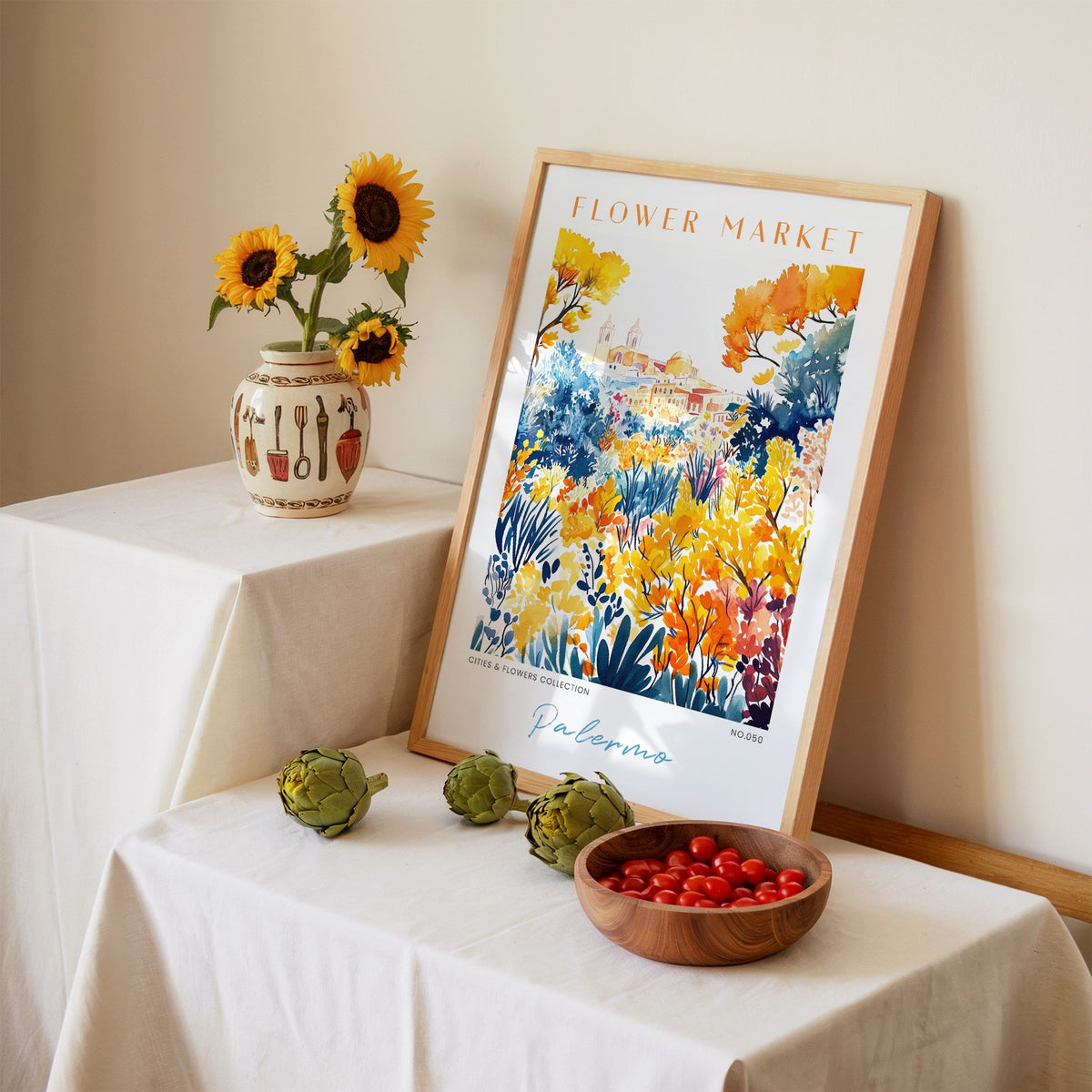 Palermo flower market print in an oak frame leaning on a linen-draped table beside a vase of sunflowers