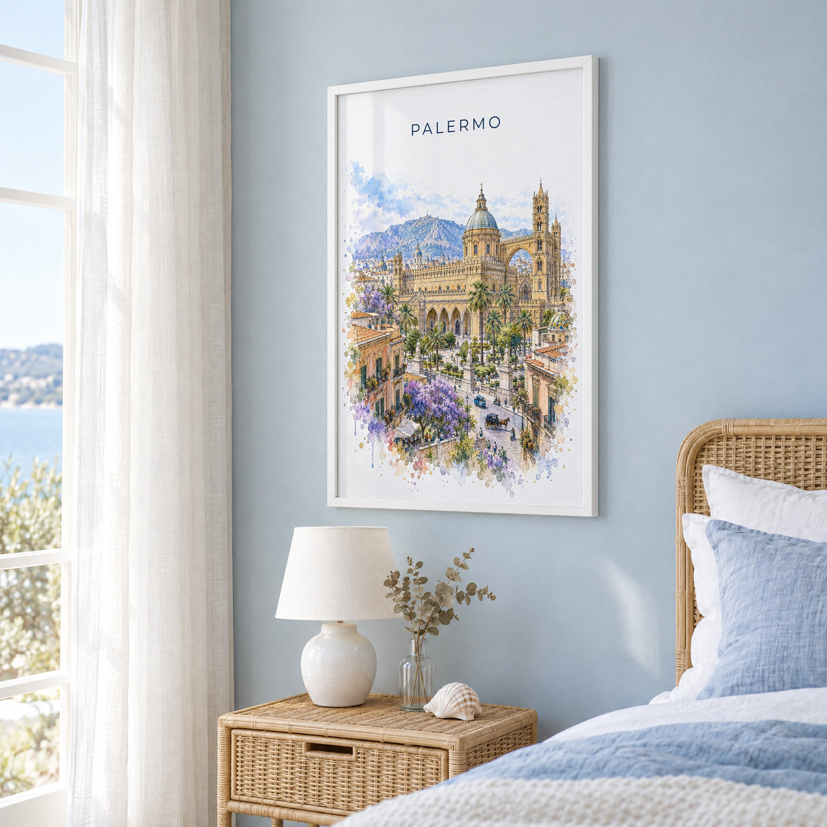Palermo watercolor print in a white frame on a pale blue wall beside a rattan bed in a coastal bedroom