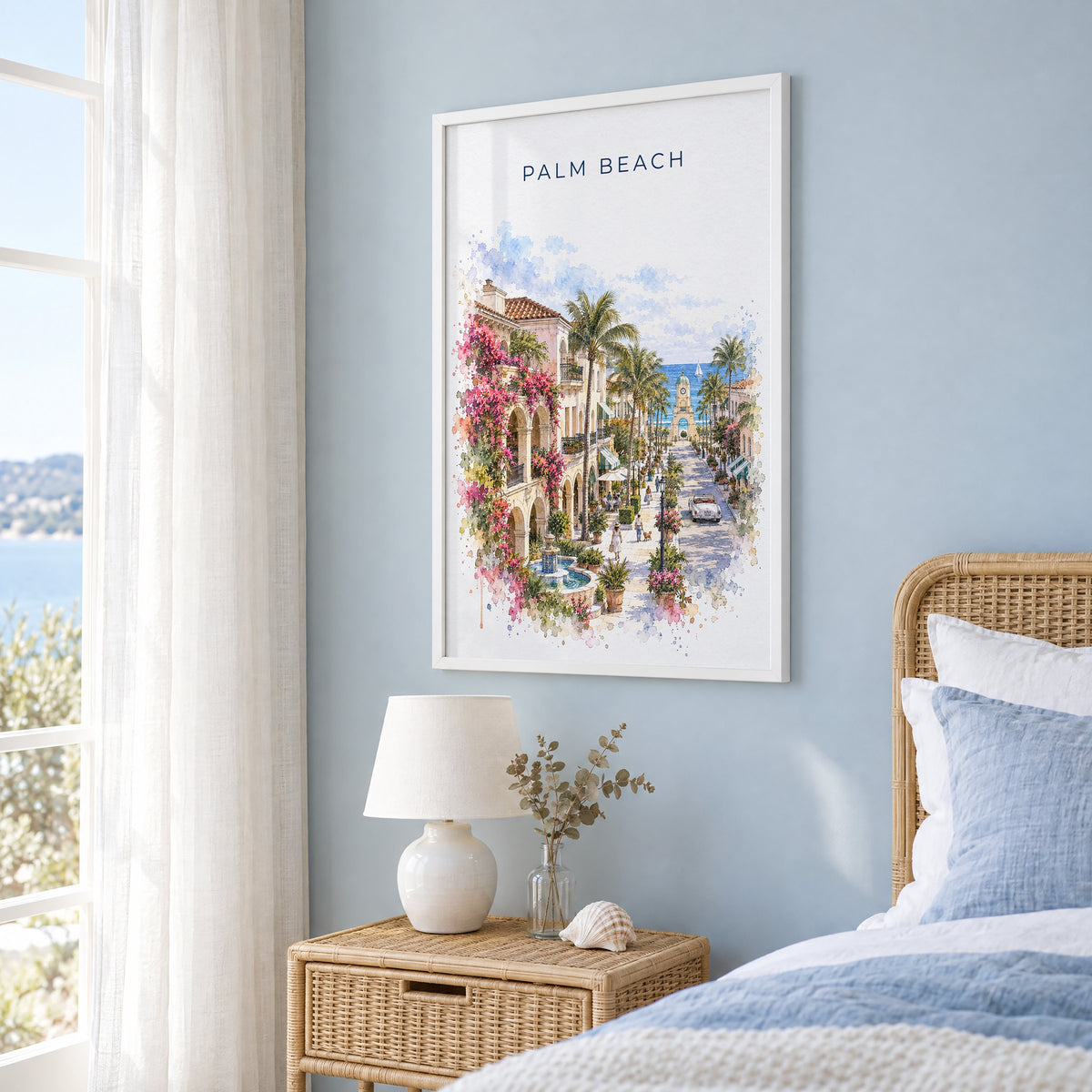 Palm Beach, Florida watercolor print in a white frame on a pale blue wall beside a rattan bed in a coastal bedroom