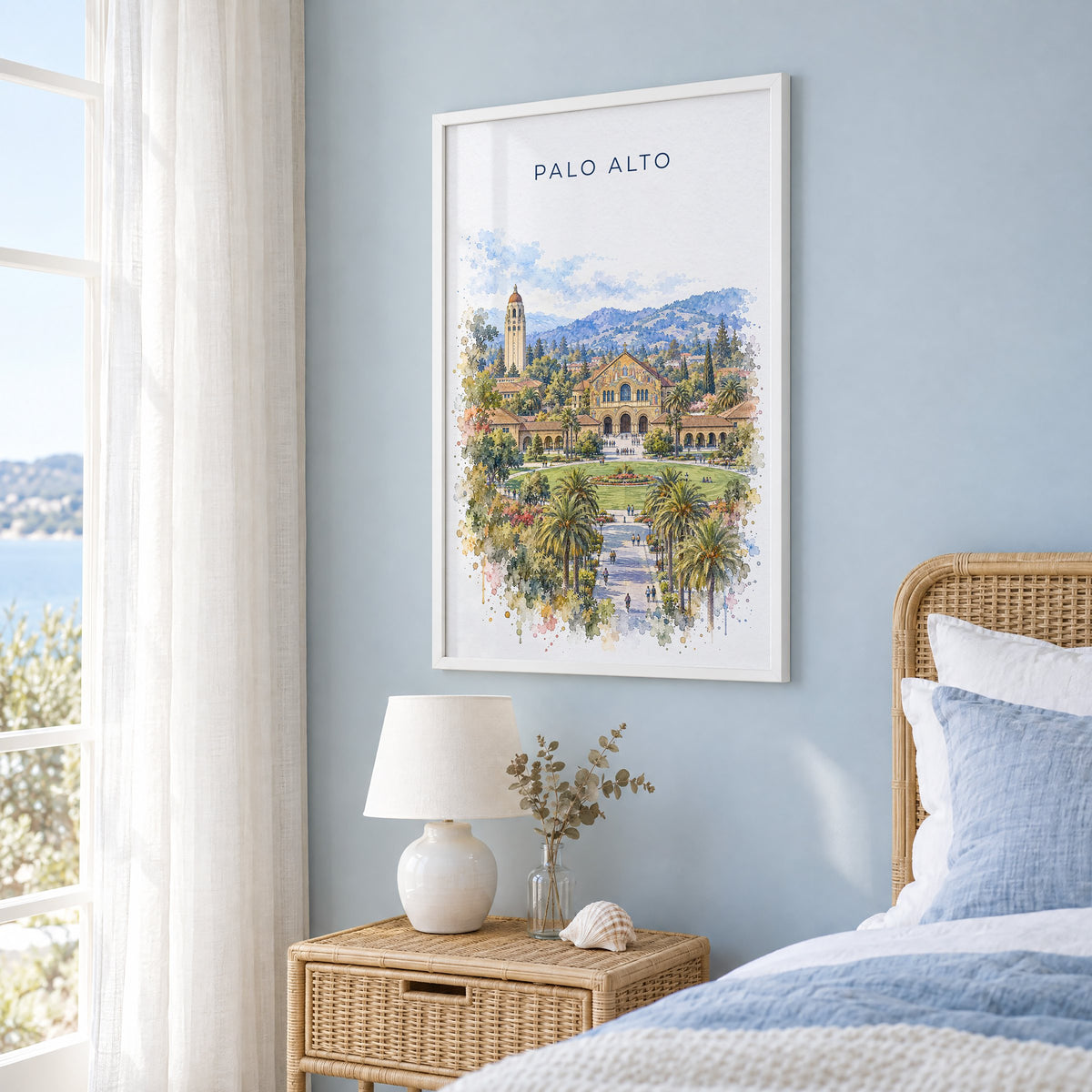 Palo Alto watercolor print in a white frame on a pale blue wall beside a rattan bed in a coastal bedroom