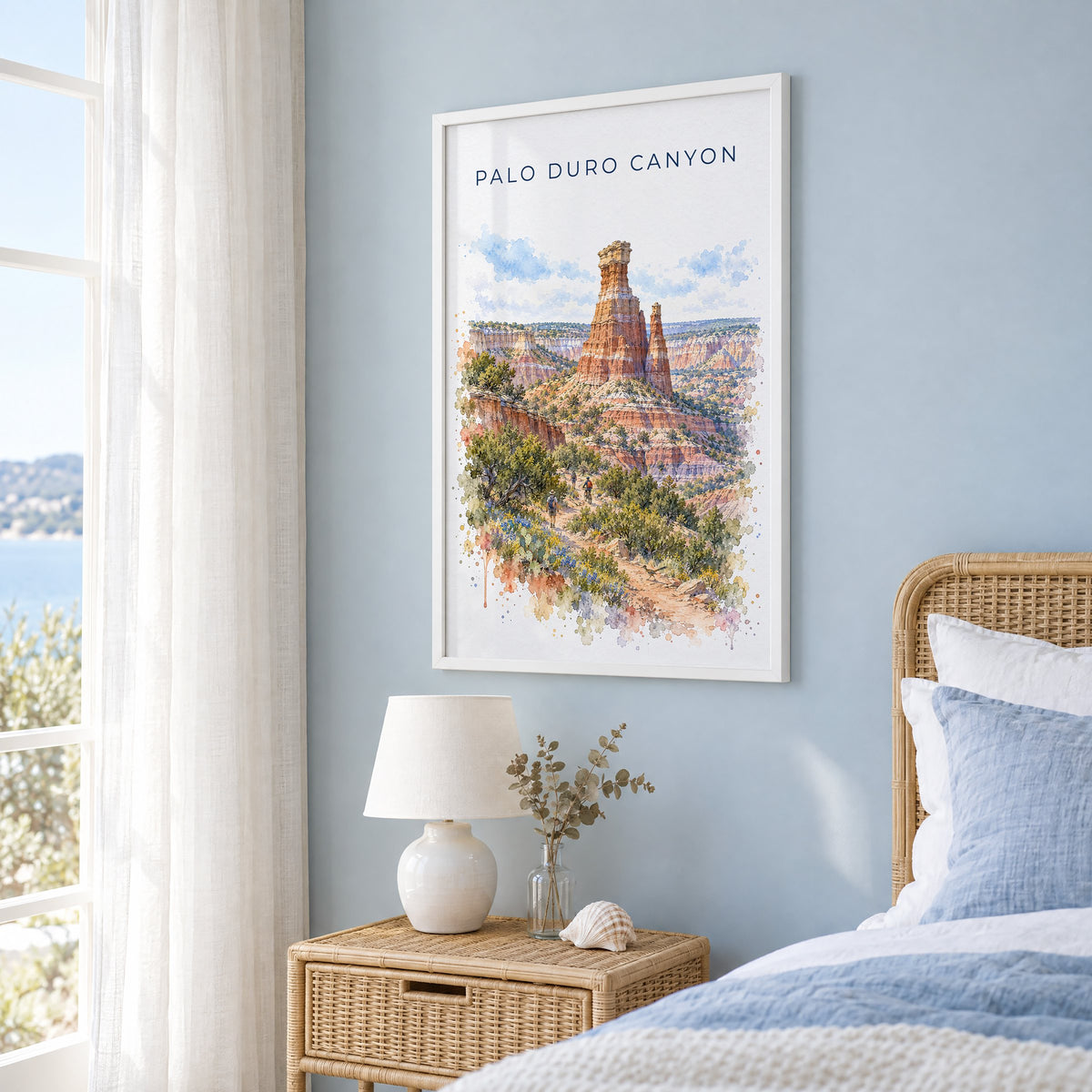 Palo Duro Canyon watercolor print in a white frame on a pale blue wall beside a rattan bed in a coastal bedroom