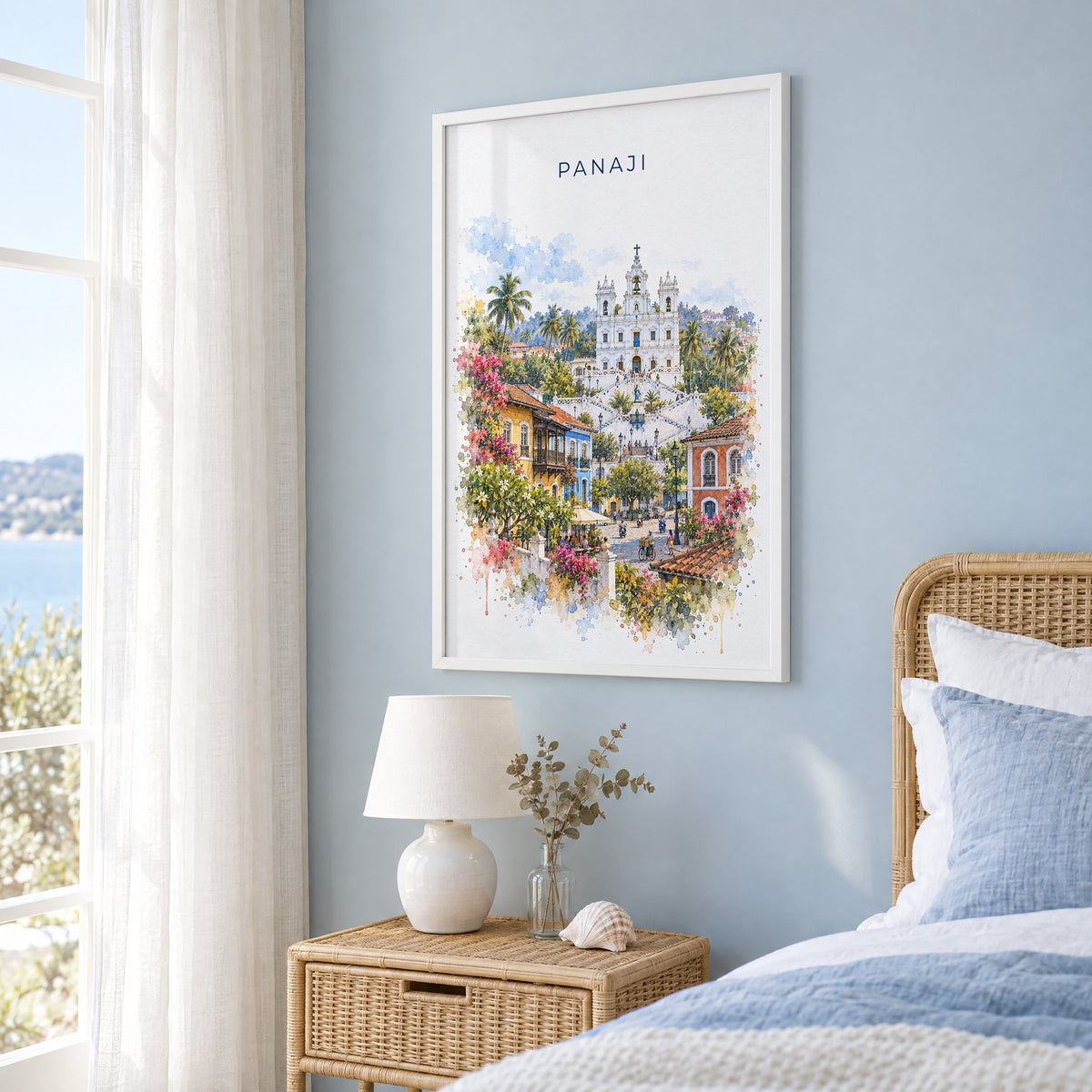 Panaji watercolor print in a white frame on a pale blue wall beside a rattan bed in a coastal bedroom