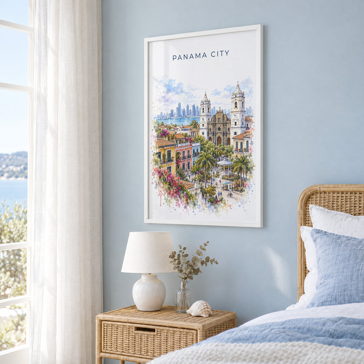 Panama City, Panama watercolor print in a white frame on a pale blue wall beside a rattan bed in a coastal bedroom