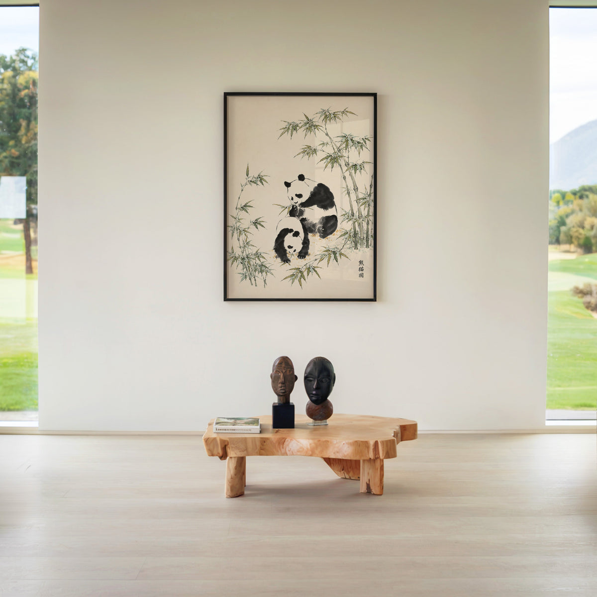 two pandas with bamboo ink painting print in a black frame above a live-edge wood coffee table between garden windows