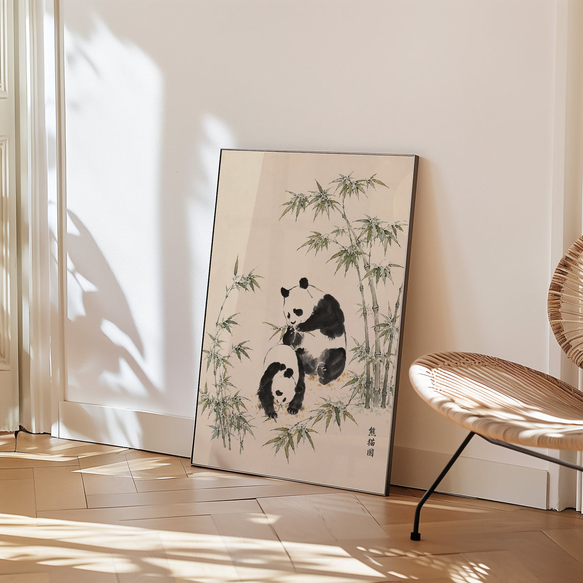 two pandas with bamboo ink painting print in a black frame leaning on a herringbone floor beside a woven rattan chair