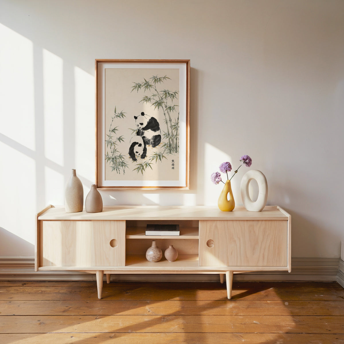 two pandas with bamboo ink painting print shown in a wood frame with a white mat above a pale wood media console