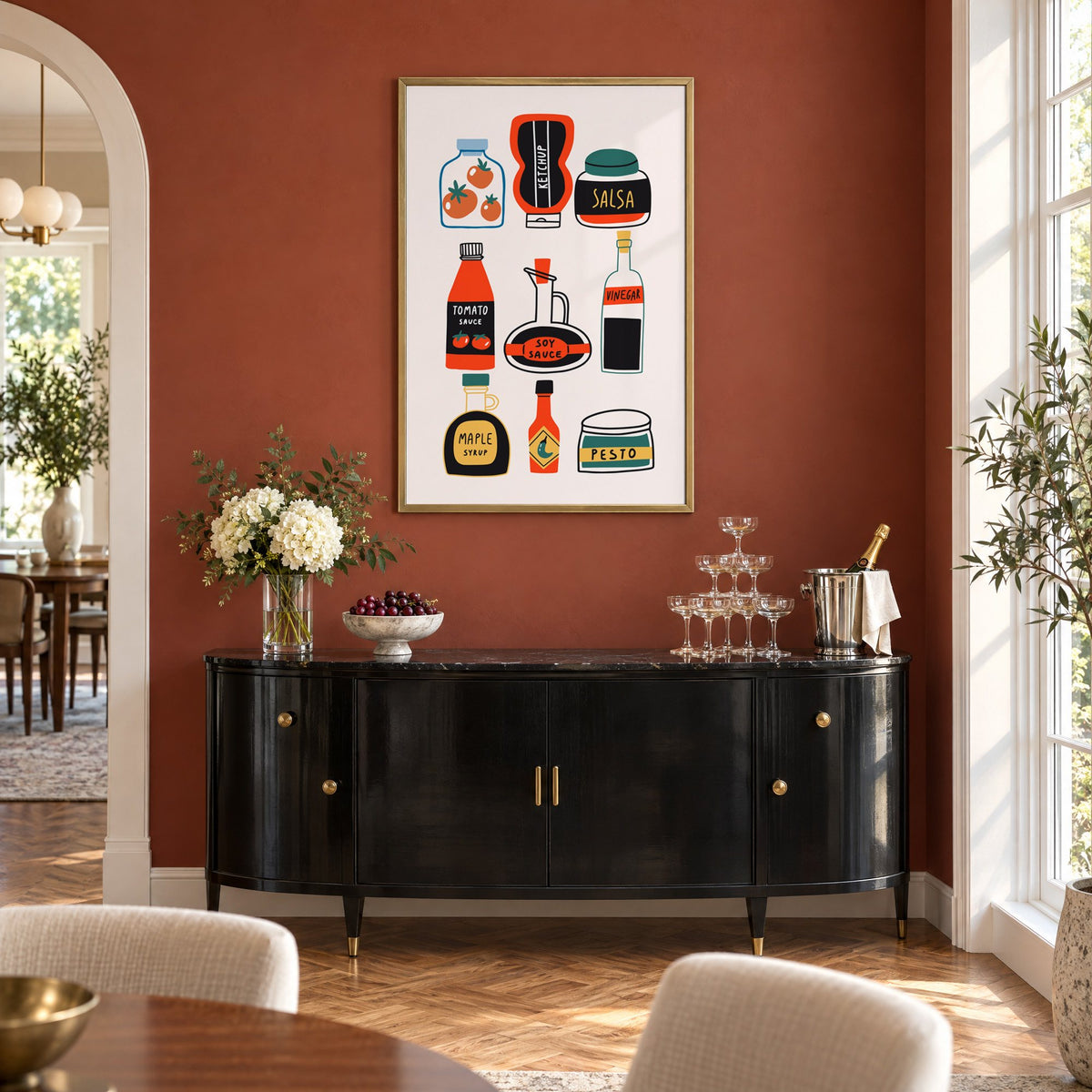 Pantry sauces bottles and jars print in a brass frame on a terracotta wall above a black buffet with a champagne tower