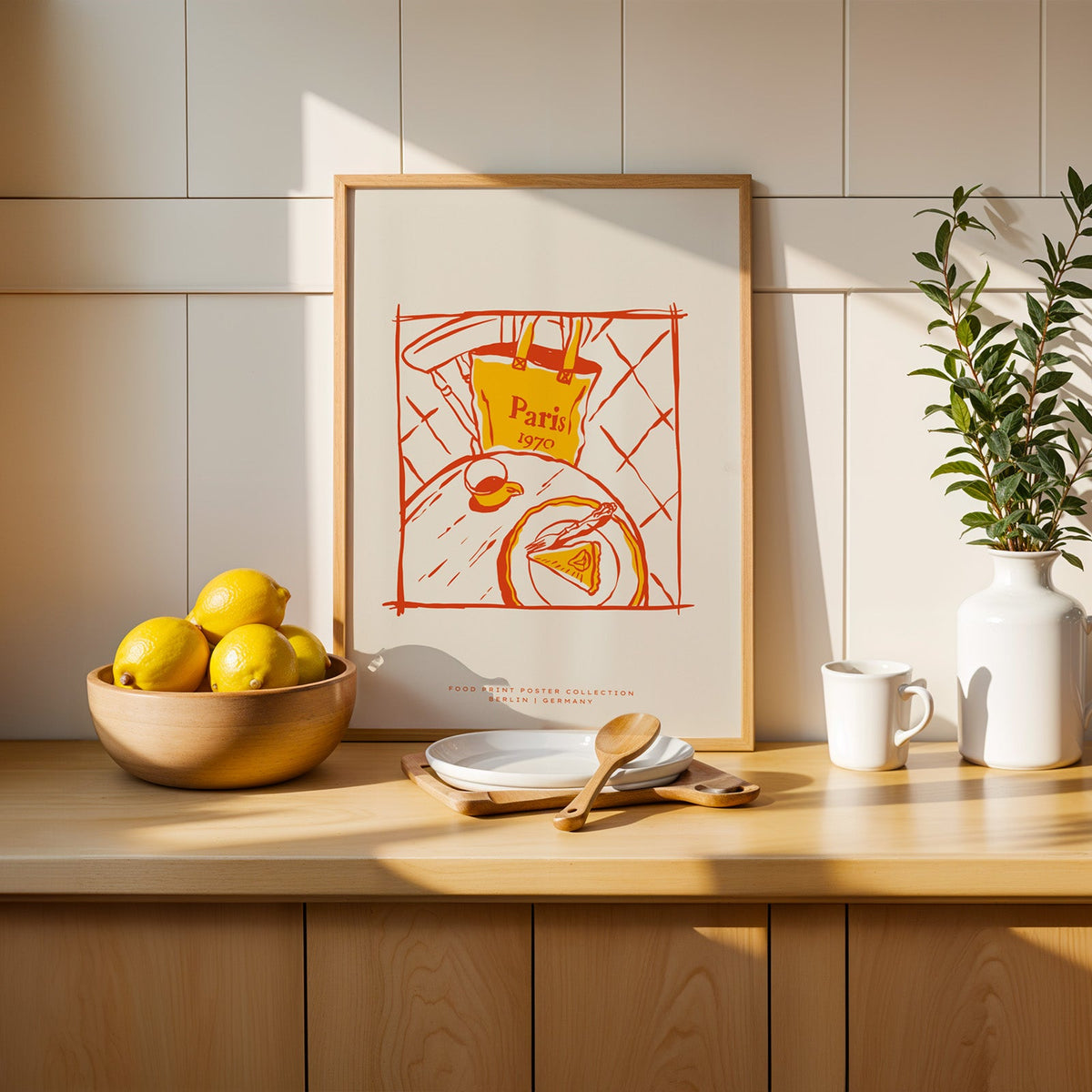 Paris cafe table print in a slim oak frame leaning on a counter beside a bowl of lemons