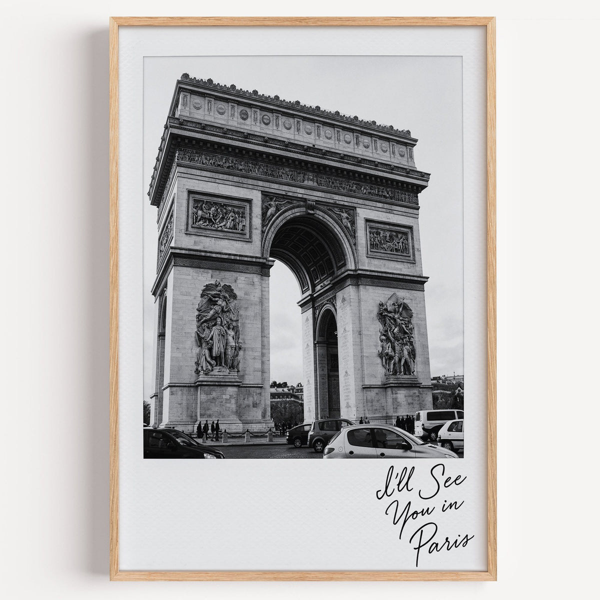 Arc de Triomphe instant photo with Paris script print in a light oak frame on a plain white wall
