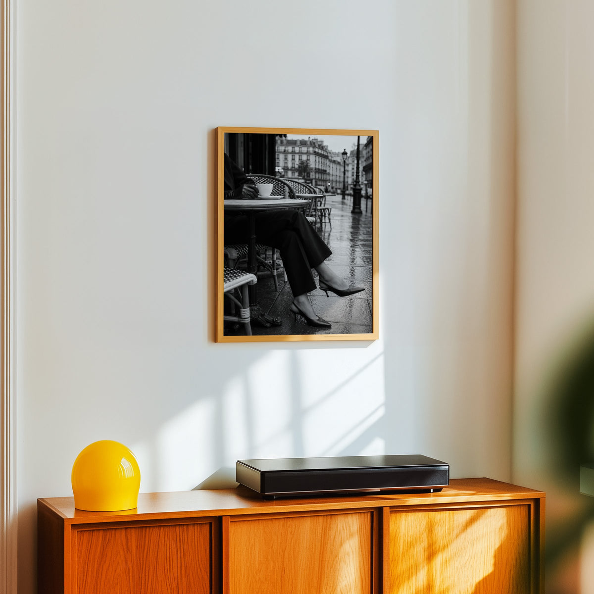 Black heels at rainy Paris café table print in an oak frame above a teak sideboard with a yellow glass lamp