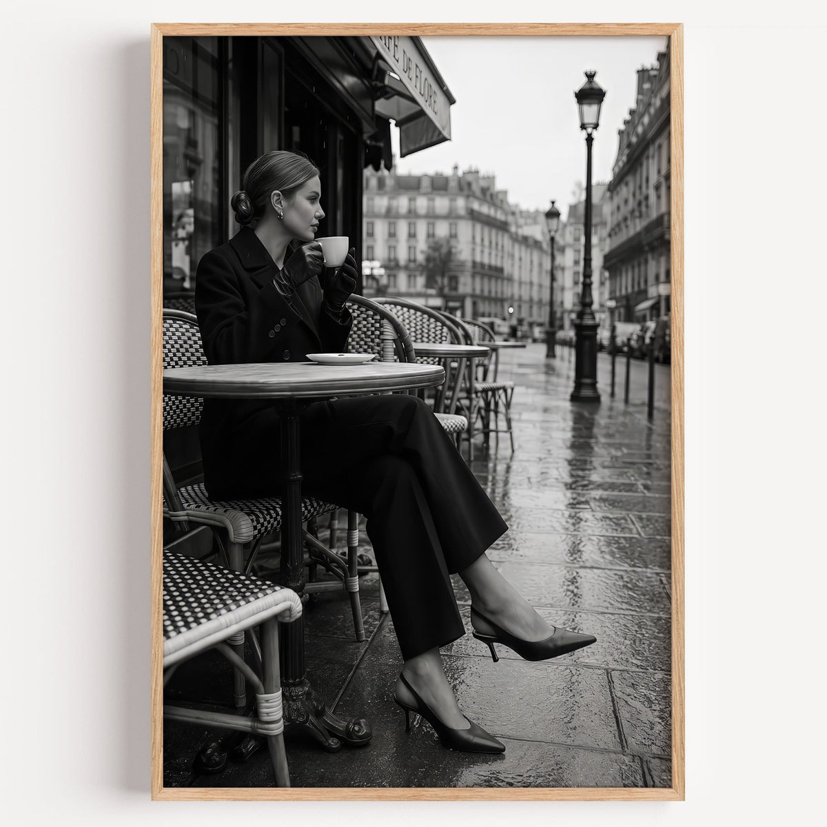 Black and white Paris cafe woman with coffee print in a light oak frame on a plain white wall