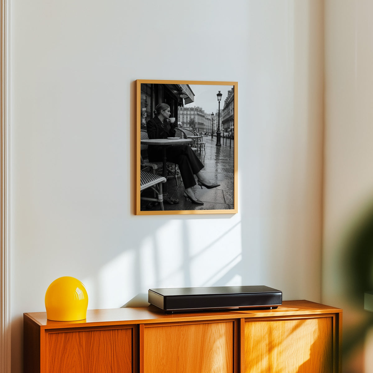 Black and white Paris cafe woman with coffee print in an oak frame above a teak sideboard with a yellow glass lamp