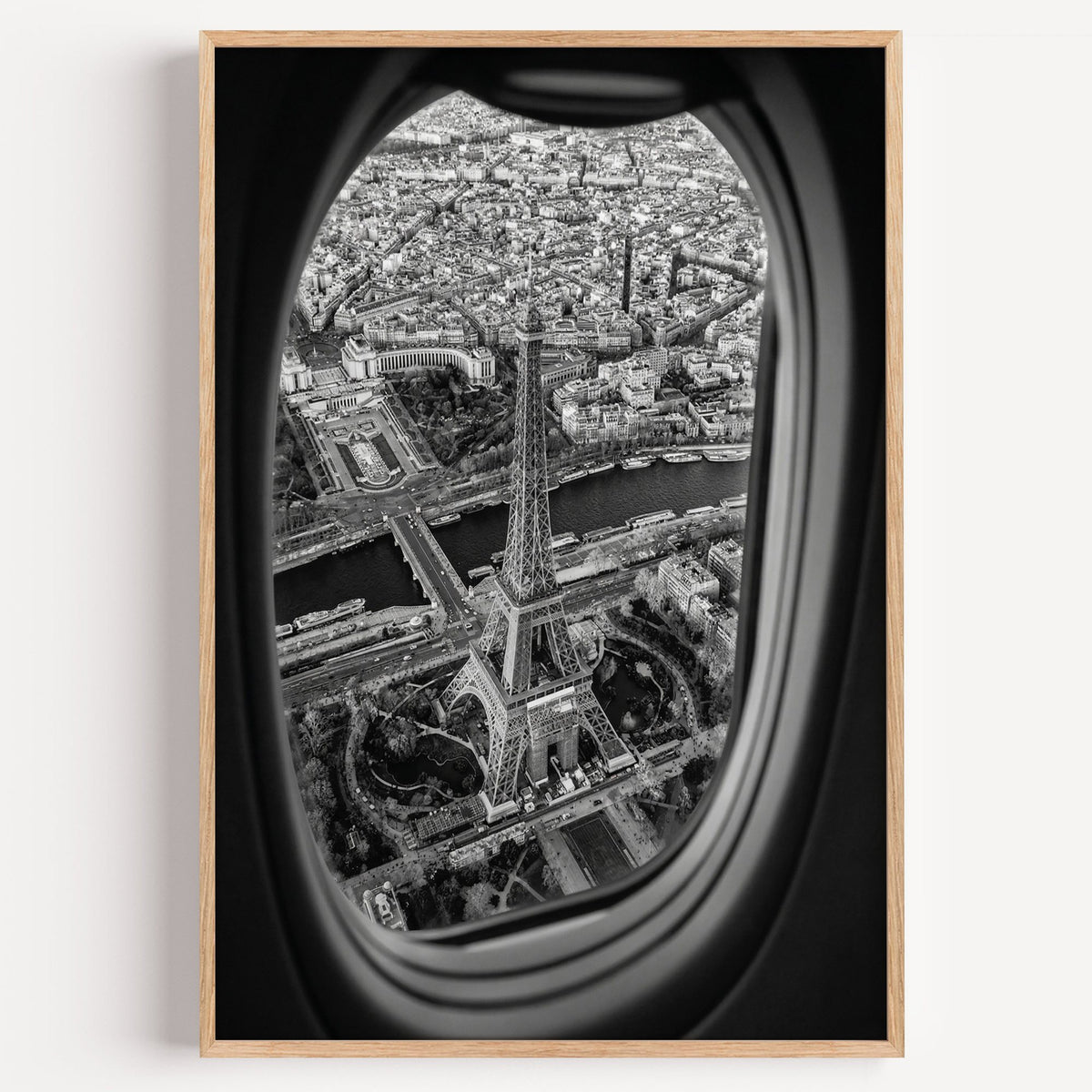 Eiffel Tower seen through an airplane window print in a light oak frame on a plain white wall