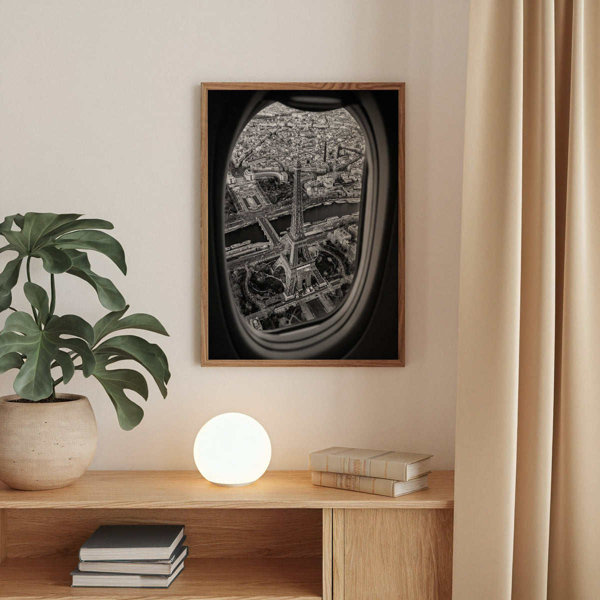 Eiffel Tower seen through an airplane window print in a walnut frame above an oak cabinet with a glowing globe lamp