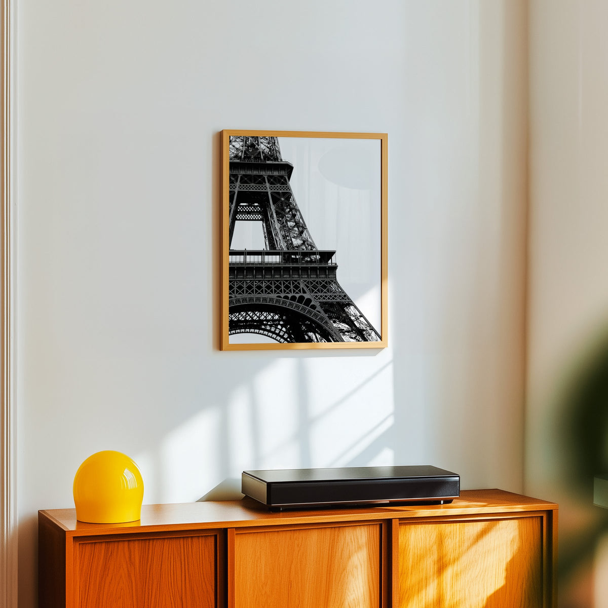 Eiffel Tower close-up on white background print in an oak frame above a teak sideboard with a yellow glass lamp