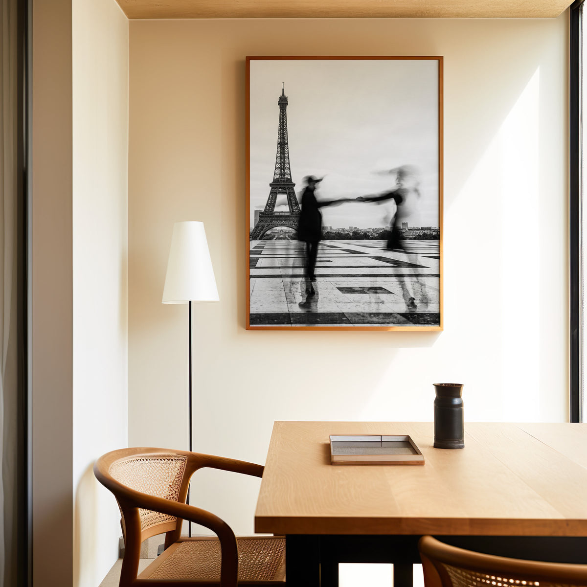 Blurred couple twirling near the Eiffel Tower print in an oak frame above a dining table and cane chair
