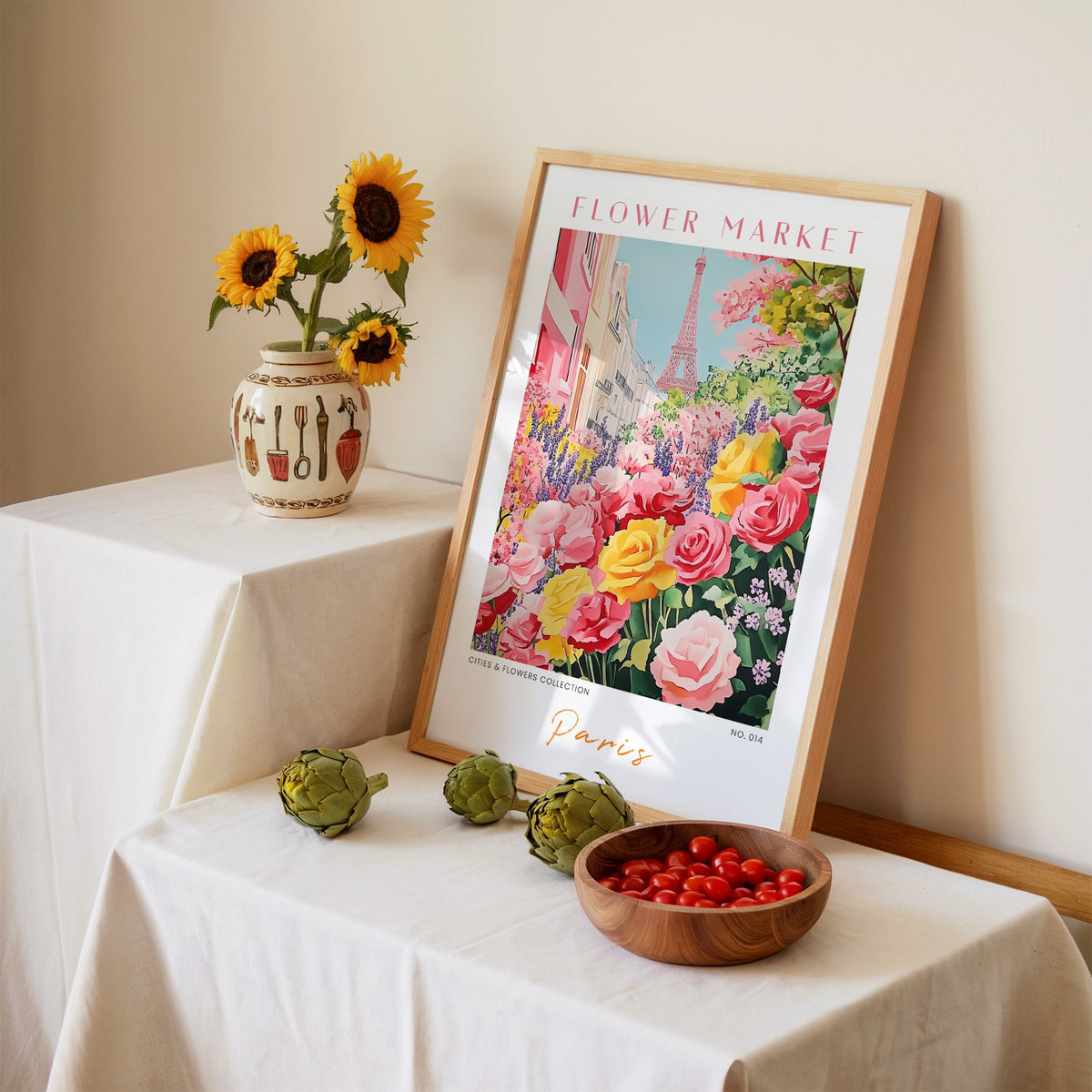 Paris flower market print in an oak frame leaning on a linen-draped table beside a vase of sunflowers