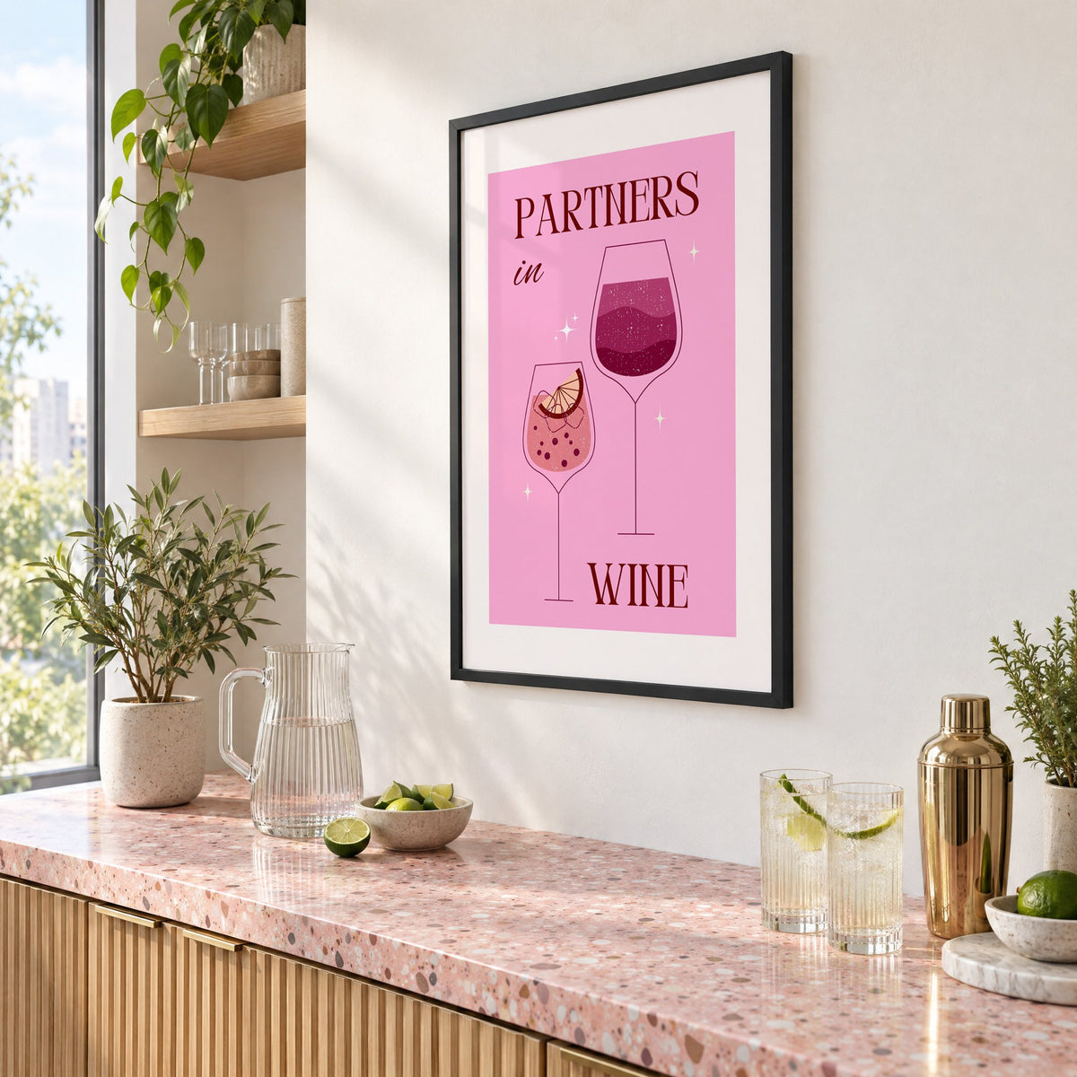 Partners in Wine two glasses pink print in a black frame above a pink terrazzo cocktail counter with limes, seen at an angle