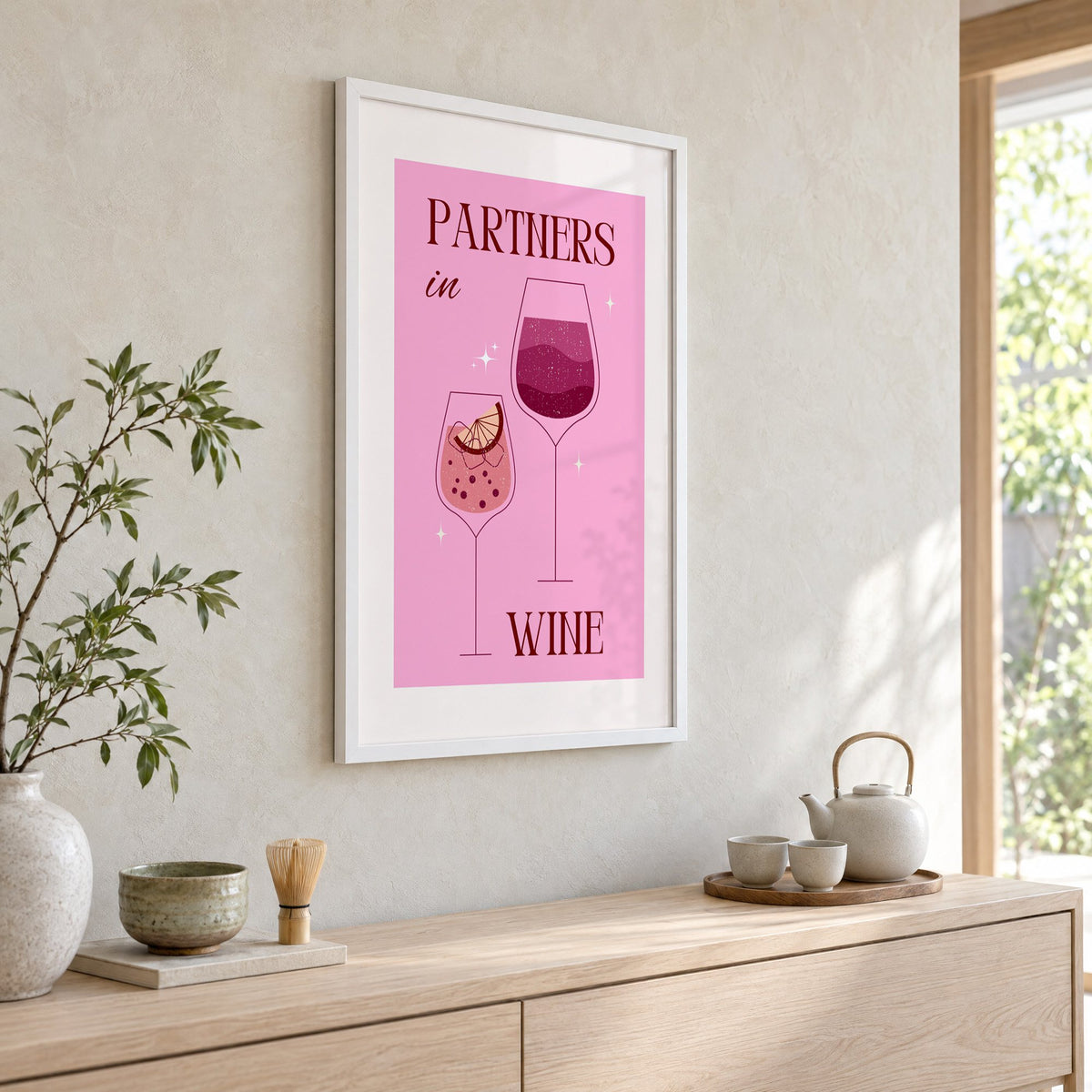 Partners in Wine two glasses pink print in a white frame above a pale wood console with a matcha tea set