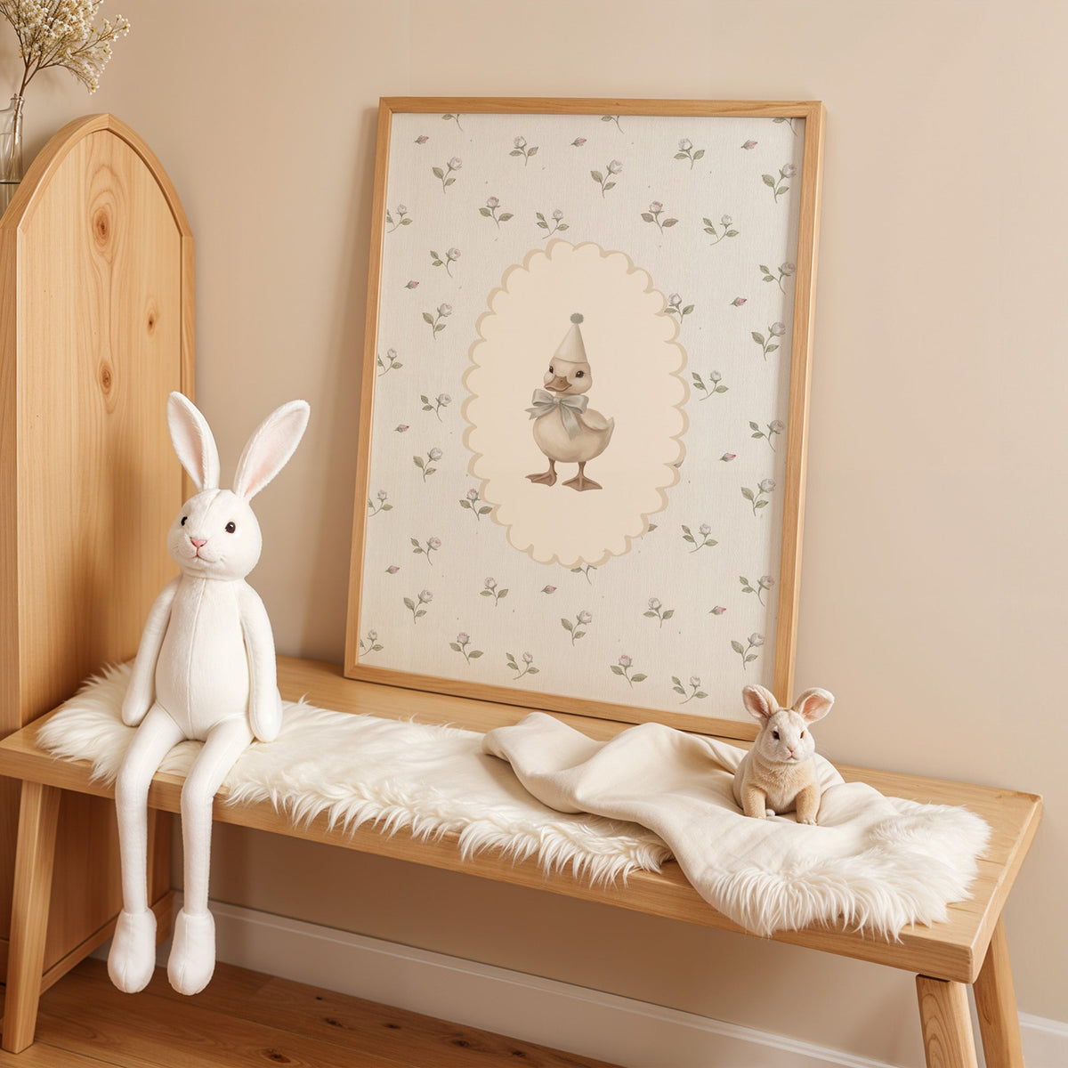Party duckling in cream oval on rosebuds nursery print in an oak frame on a sheepskin bench beside a white plush bunny