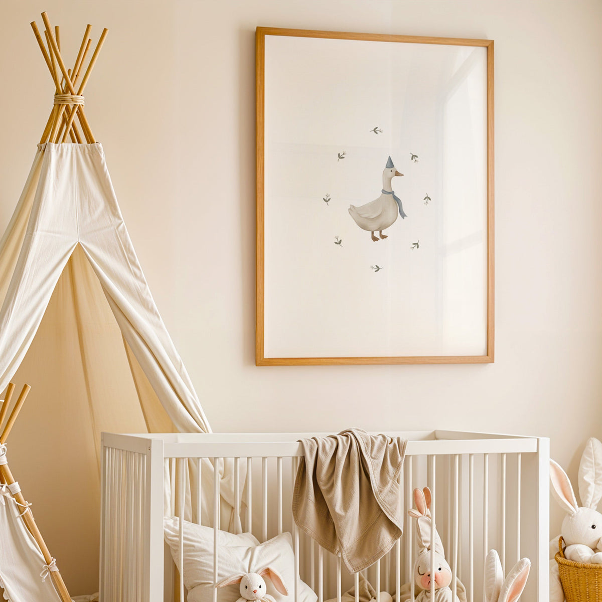 Goose in a blue party hat and scarf nursery print in an oak frame above a white crib beside a canvas teepee