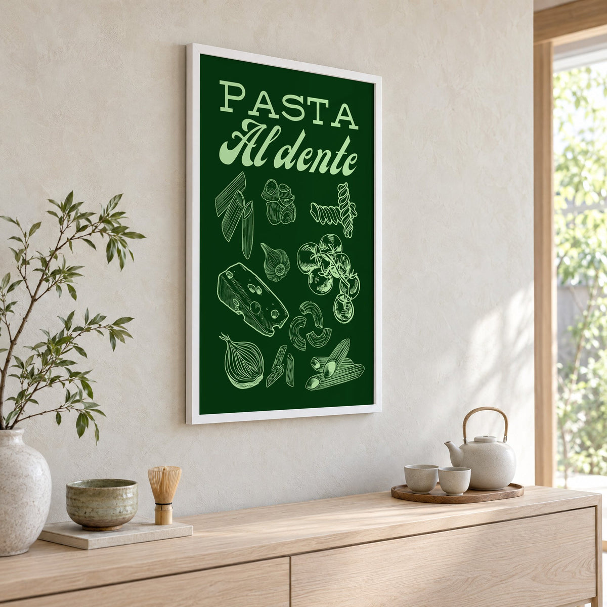 Pasta Al dente engraved green print in a white frame above a pale wood console with a matcha tea set