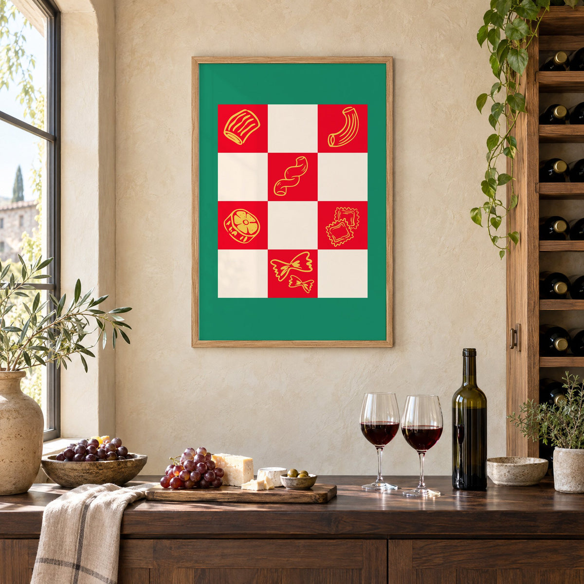 Red checkerboard pasta shapes print with green border in an oak frame on a limewashed wall above a wine counter with red wine, cheese and grapes