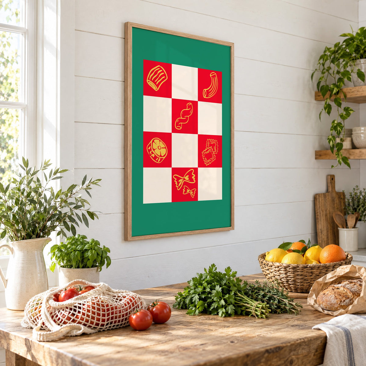 Red checkerboard pasta shapes print with green border in an oak frame on a shiplap wall above a farm table with market tomatoes and citrus, seen at an angle