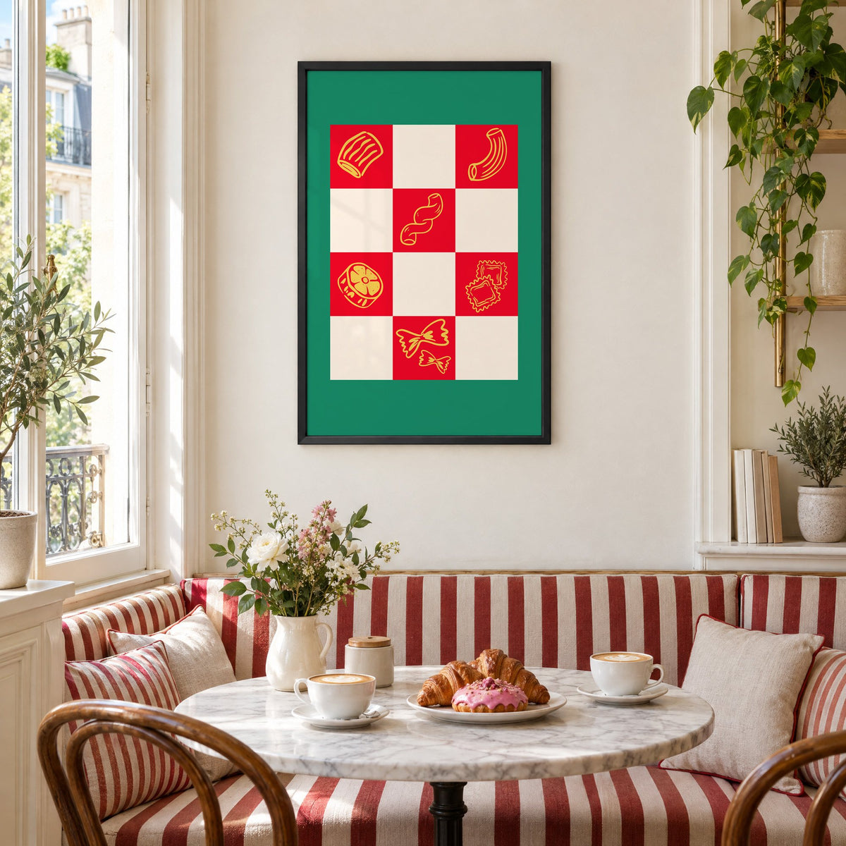 Red checkerboard pasta shapes print with green border in a black frame above a striped cafe breakfast nook with cappuccino and pastries