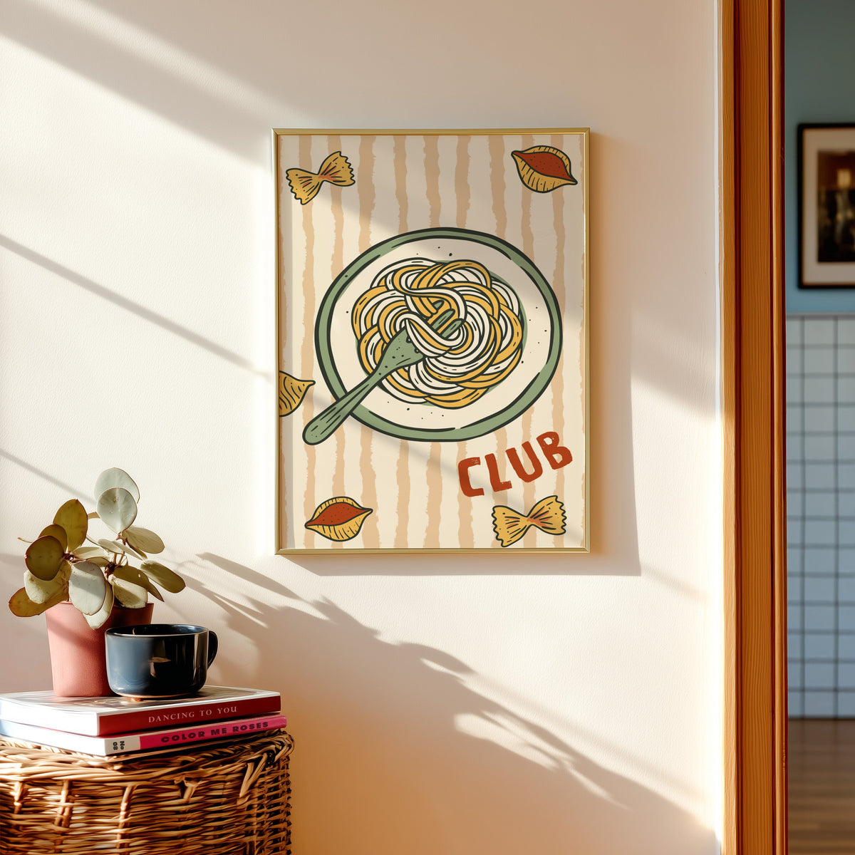 Pasta Club print in a gold frame above a basket of books and a pilea plant