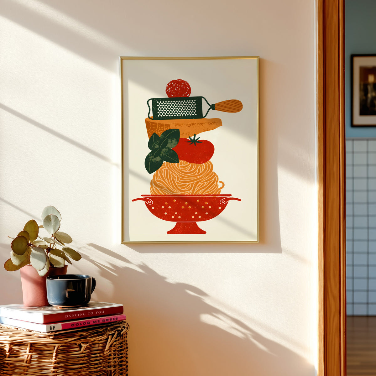 Pasta colander print in a gold frame above a basket of books and a pilea plant