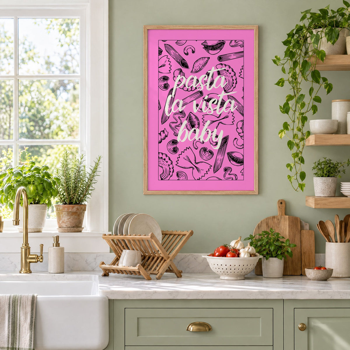 Pasta la vista baby pink print in an oak frame on a sage green kitchen wall beside a farmhouse sink and herbs