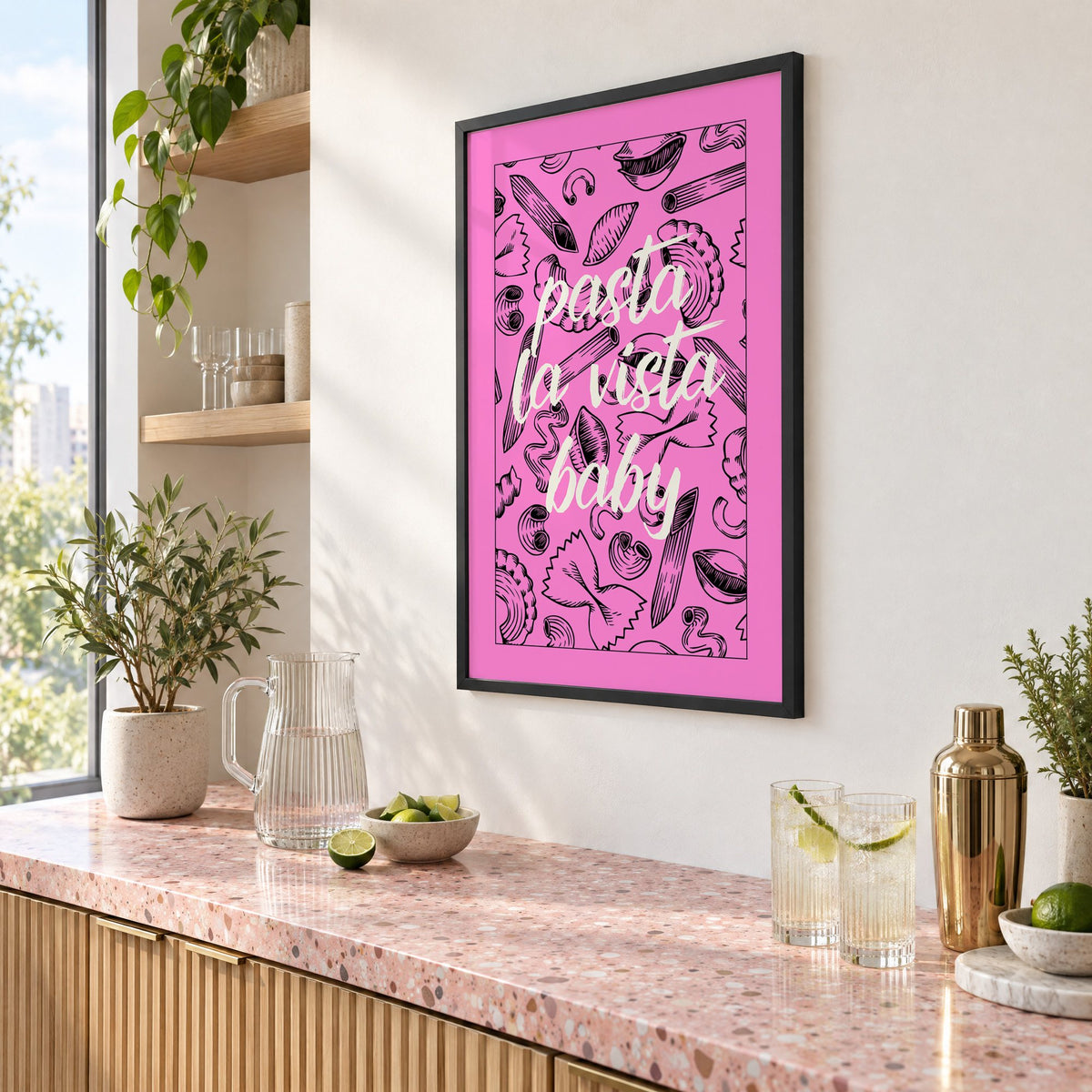 Pasta la vista baby pink print in a black frame above a pink terrazzo cocktail counter with limes, seen at an angle