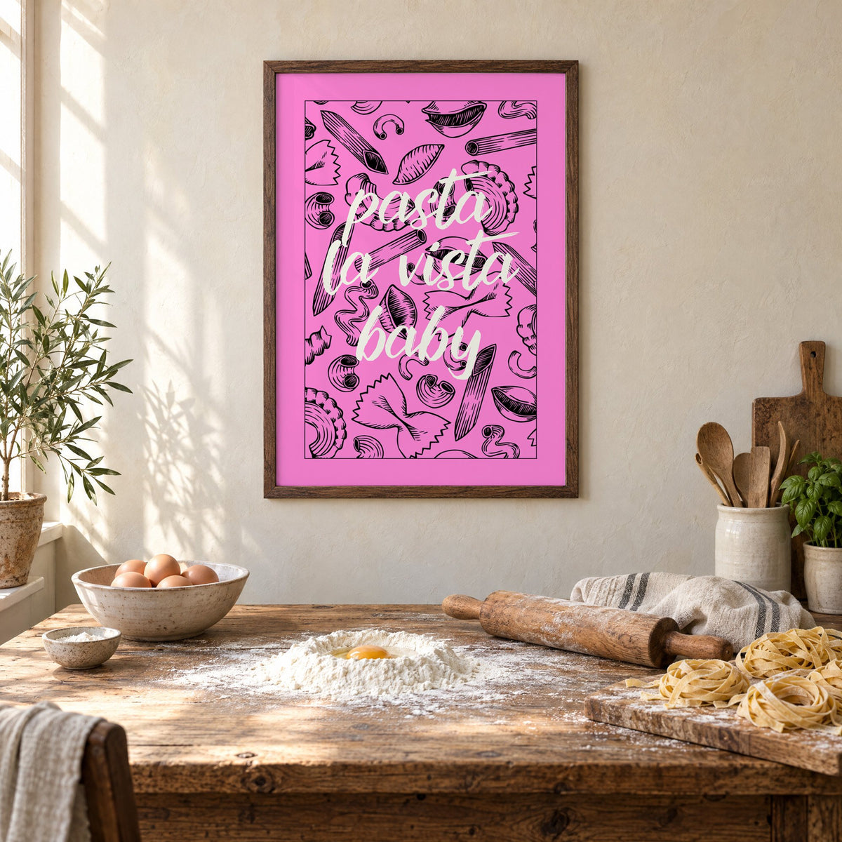 Pasta la vista baby pink print in a walnut frame above a rustic table set for making fresh pasta